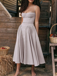 Ruched sweetheart neck cami dress in light beige, featuring a flowy skirt and adjustable straps, set in a rustic environment.