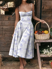 Model wearing a ruched sweetheart neck cami dress with floral design, holding a basket of vegetables.