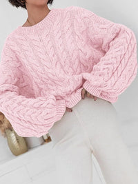 Pink cable knit long sleeve sweater with oversized sleeves, paired with light-colored bottoms.