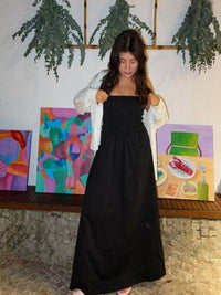 a woman in a long black dress standing in front of paintings