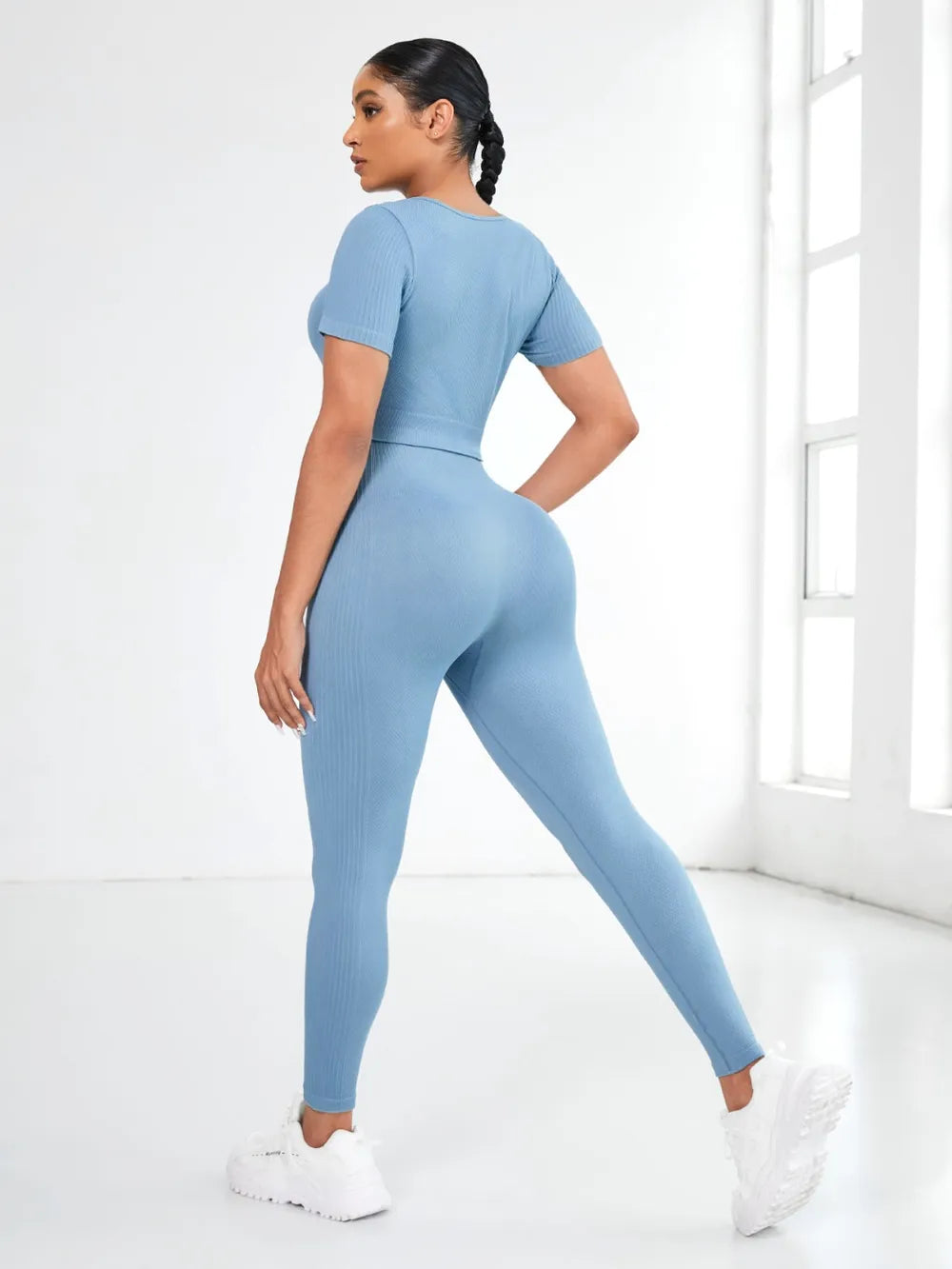 Model wearing a blue round neck short sleeve top and leggings active set from the back in a bright room.