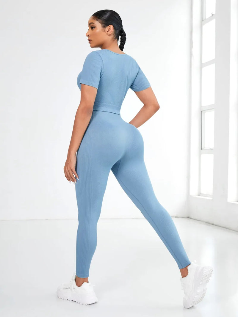 Model wearing a blue round neck short sleeve top and leggings active set from the back in a bright room.
