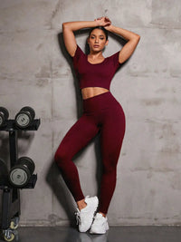 Model wearing a burgundy round neck short sleeve top and leggings active set, posing next to a rack of dumbbells.