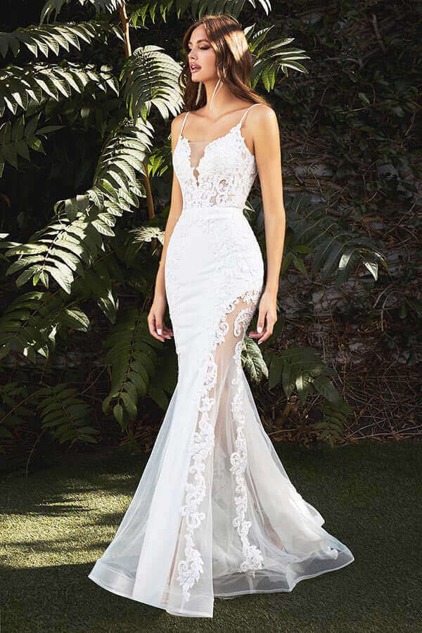 Elegant woman in white lace mermaid wedding gown/dress  with spaghetti straps and sheer panels standing outdoors in lush garden.