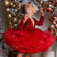 a little girl in a red dress standing in front of a christmas tree