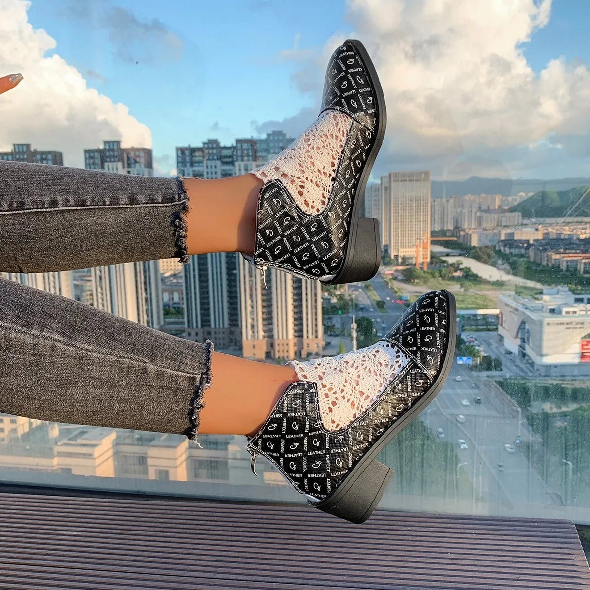 Printed point toe block heel boots in black and white, paired with distressed jeans against a city skyline backdrop.