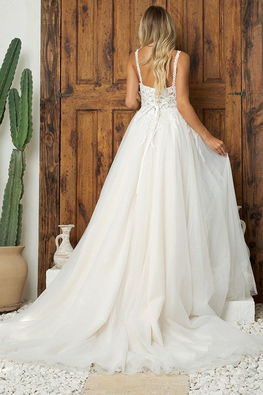 Bride in elegant A-line wedding dress with lace appliqués and chapel train standing before wooden doors.