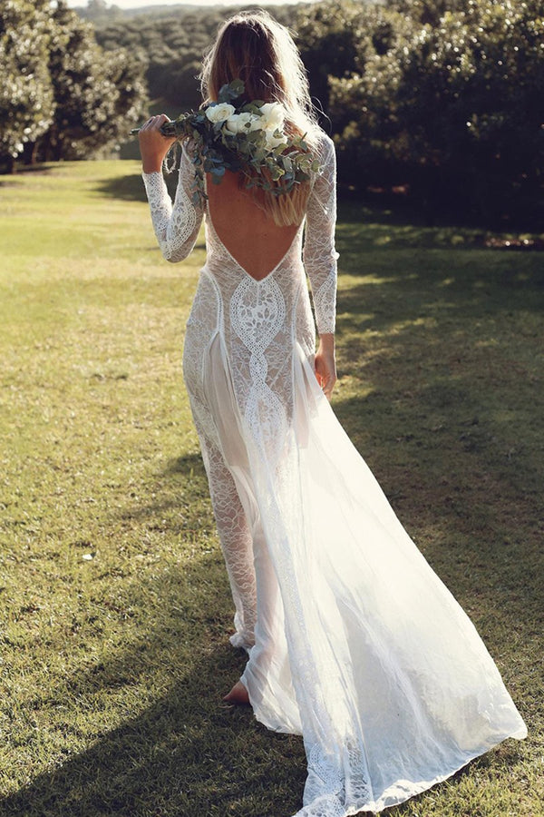 Woman wearing boho backless maxi gown in white lace, standing on a grassy field holding flowers.