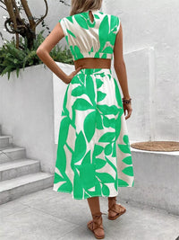 Back view of a woman wearing a green and white cutout printed sleeveless dress in a modern outdoor setting.