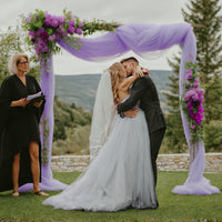 a bride and groom kissing under a wedding arch