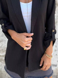 Close-up of a woman wearing a black lapel collar blazer over a white tank top, showcasing buttoned sleeves.