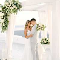 a bride and groom standing under a white wedding arch
