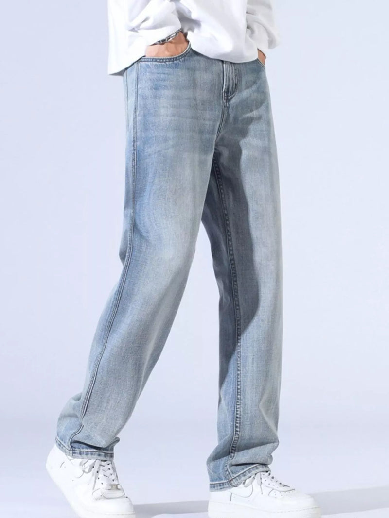 Men's relaxed fit wide leg jeans in light wash with slight stretch, styled with a casual white top and white sneakers.