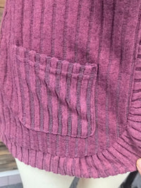 Close-up of open front ribbed knit cardigan in mauve with pocket detail and textured fabric.
