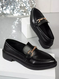Point toe black block heels loafers with gold buckle detail on a reflective surface.