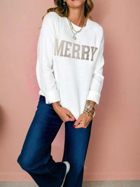 MERRY Letter Pattern Christmas Raglan Sleeve Sweater model wearing white sweatshirt and blue jeans against pink background.
