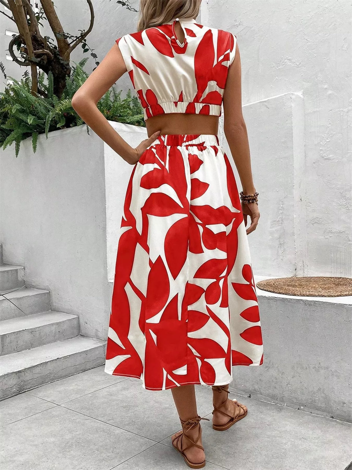 Back view of a woman in a sleeveless red and white floral cutout dress, showcasing the tied waist and skirt details.