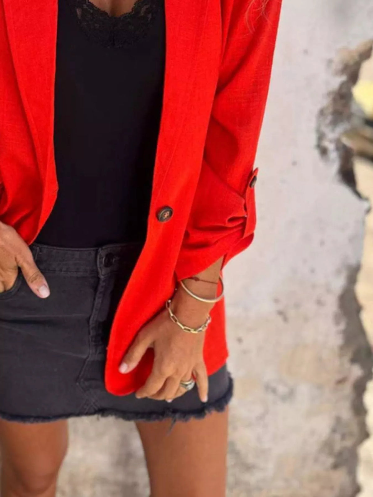 Woman wearing a red lapel collar long sleeve blazer over a black top and denim skirt.