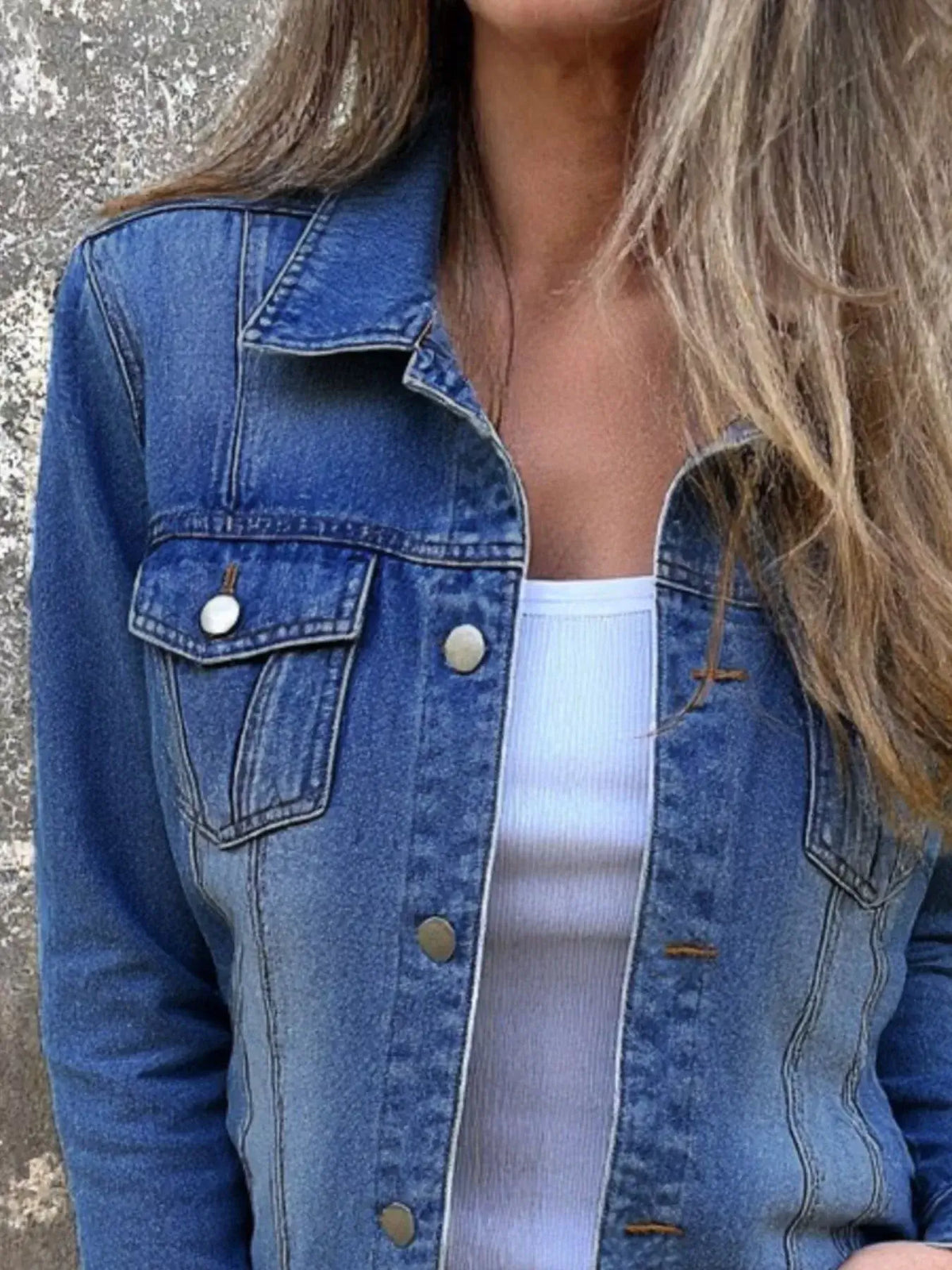 Close-up of a woman wearing a blue denim jacket with button front and long sleeves, paired with a white top.