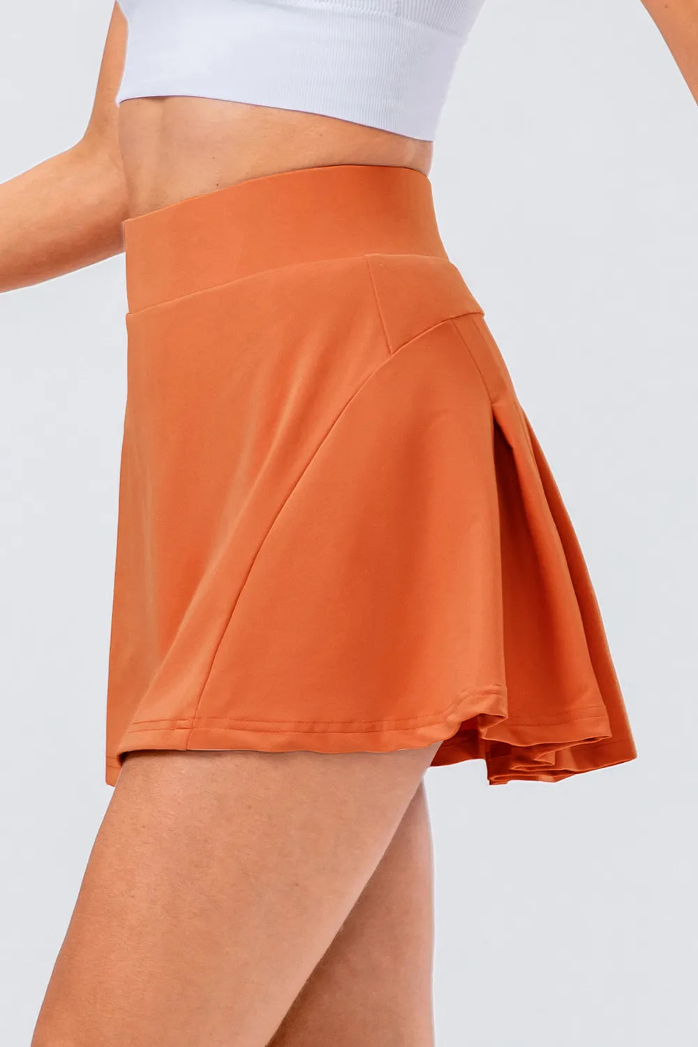High waist pleated active skirt in orange, showcasing its stretch material and flared design.