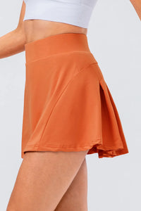 High waist pleated active skirt in orange, showcasing its stretch material and flared design.