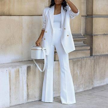 a woman in a white suit leaning against a wall