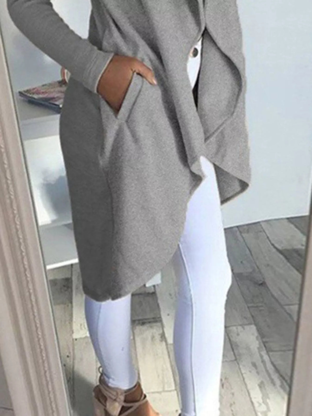 Full size lapel collar long sleeve coat in grey, featuring pockets, styled with white jeans and heels.