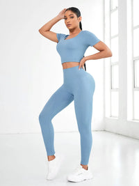 Model wearing a blue round neck short sleeve top and leggings active set in a bright indoor space.