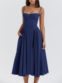 Model wearing a ruched sweetheart neck cami dress in navy blue with a flowy skirt and pockets.