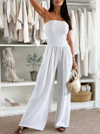 Woman wearing a smocked tube wide-leg jumpsuit in white, styled with a bag, showcasing a chic formal look.