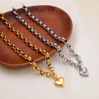 Heart Pendant Toggle Clasp Chain Necklace featuring gold and silver links elegantly displayed on a wooden plate.