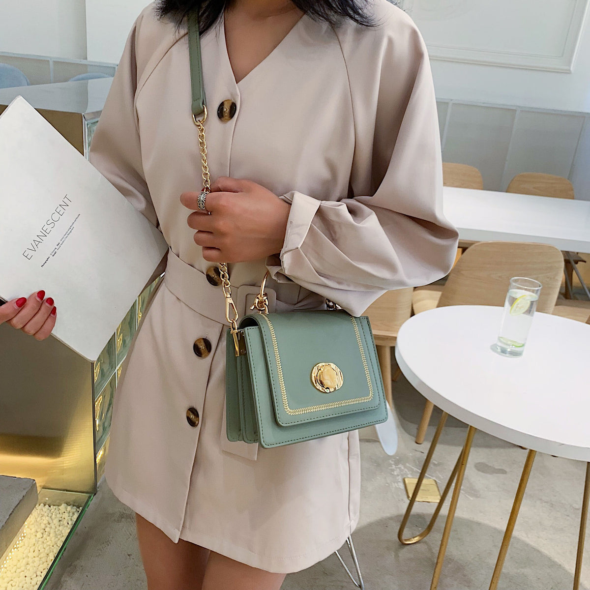 Elegant woman holding a mint green leather mini crossbody bag in a chic cafe setting.