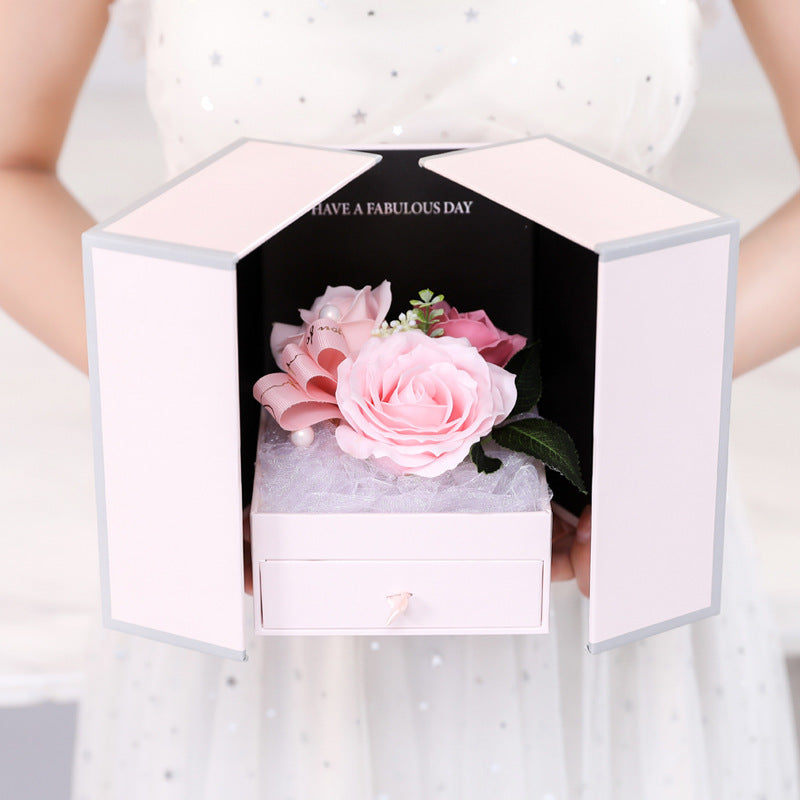 a woman holding a box with a pink flower inside of it