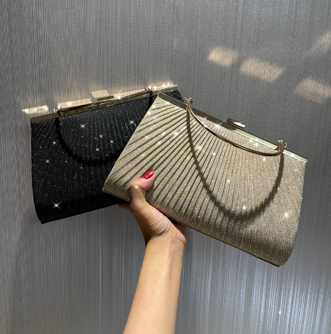 Two pleated shiny evening bags, one black and one gold, held in hand against a shimmering background.