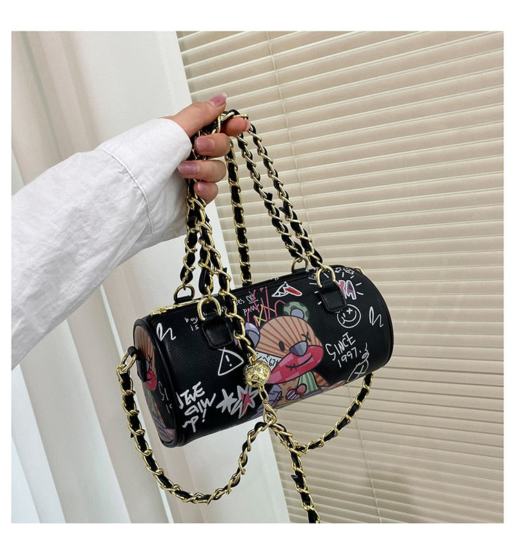Graffiti cylindrical leather zipper crossbody bag, stylish design for luxurious weddings, carried by hand with gold chain strap.