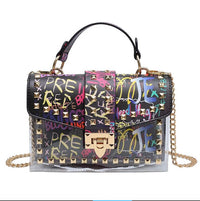 Colorful embellished handbag with graffiti print, gold studs, and a stylish chain strap for modern elegance.