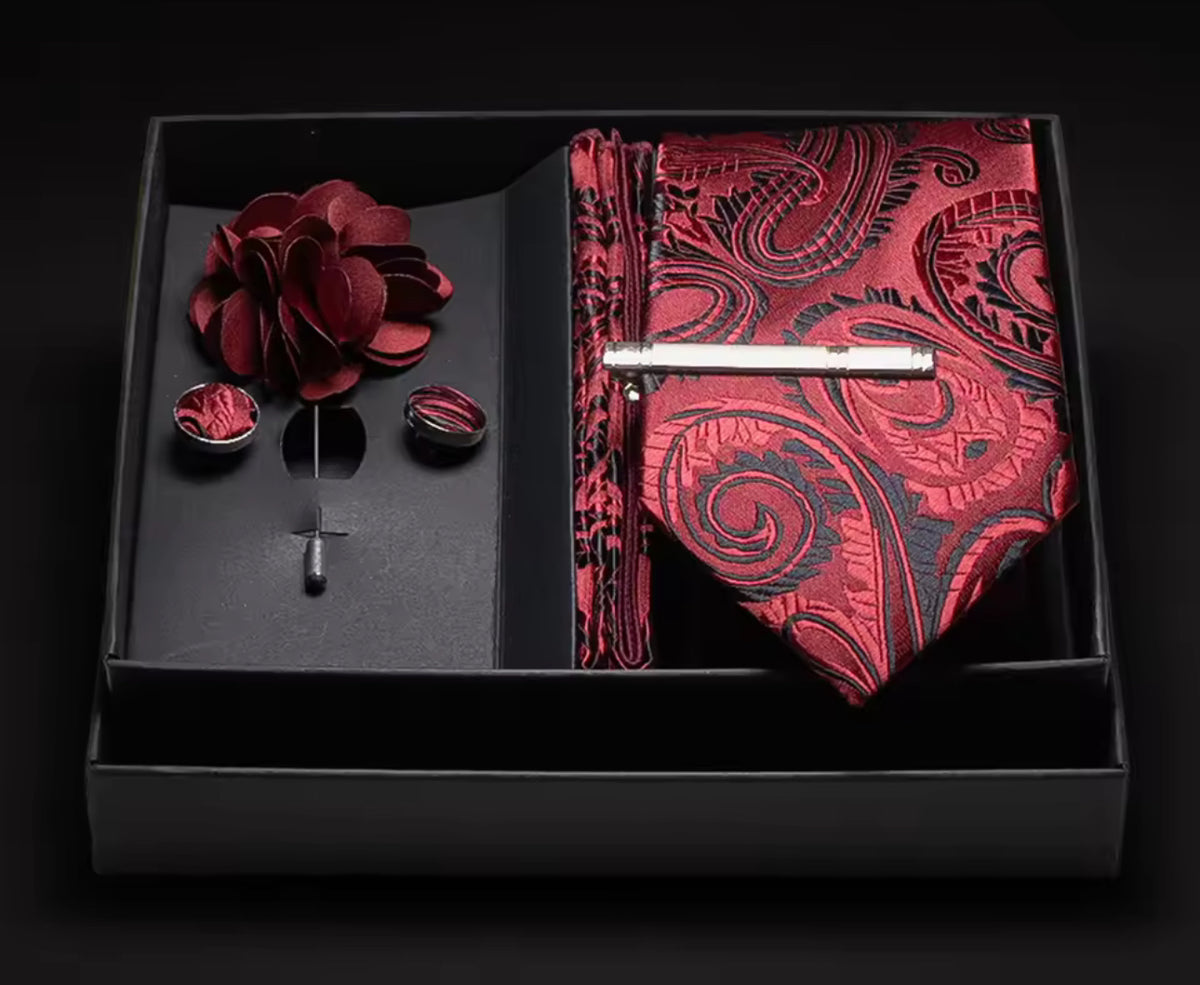 Elegant red paisley tie and pocket square set with cufflinks and floral accessory in a black box.