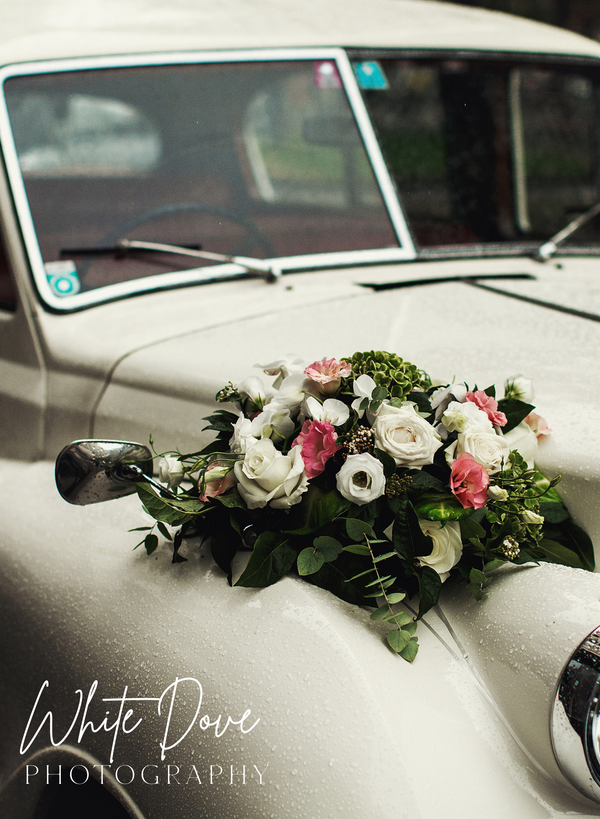 Floral arrangement on a vintage car with 'White Dove Photography' watermark.