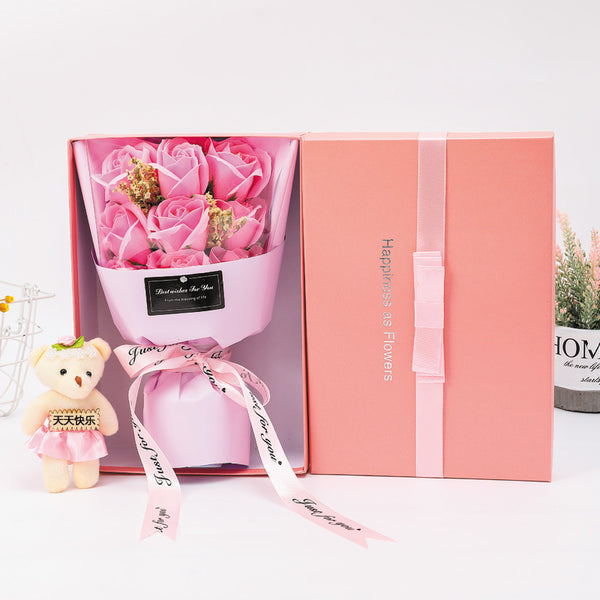 a box of pink roses with a teddy bear next to it