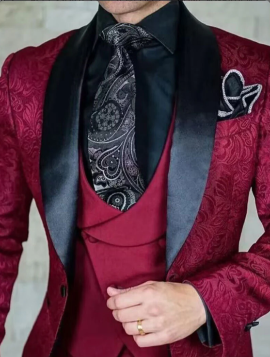 Red jacquard paisley tuxedo with black tie and pocket square, showcasing modern men's formalwear style.
