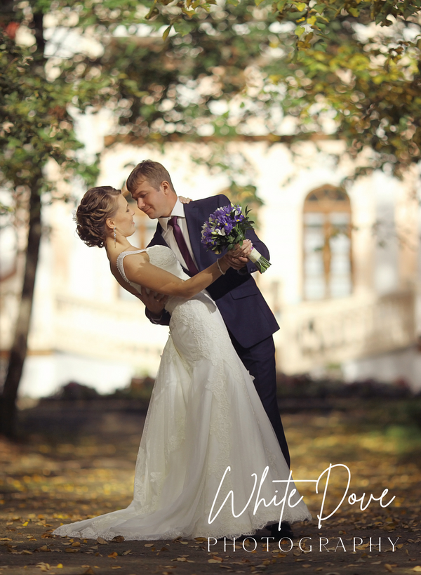 Couple in wedding attire embracing outdoors with 'White Dove Photography' watermark.