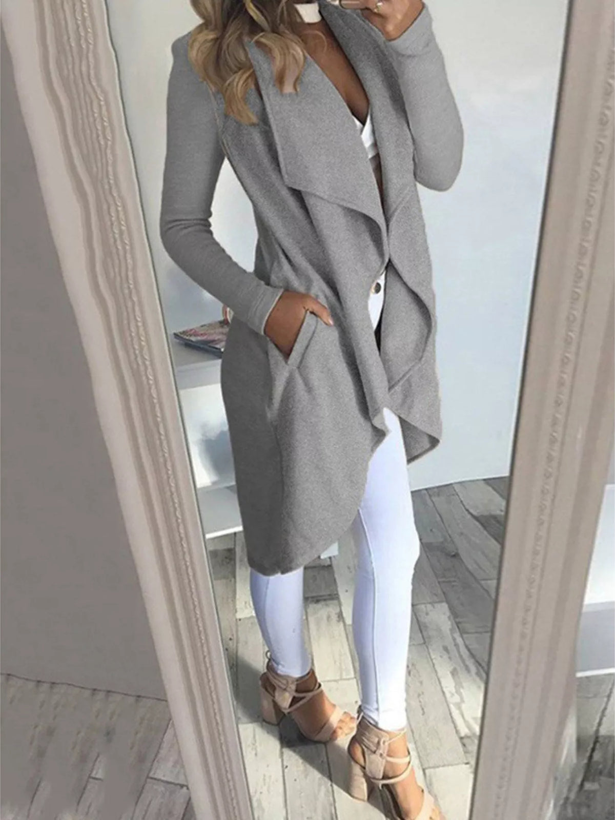 Woman wearing a grey lapel collar long sleeve coat with pockets styled over white pants.
