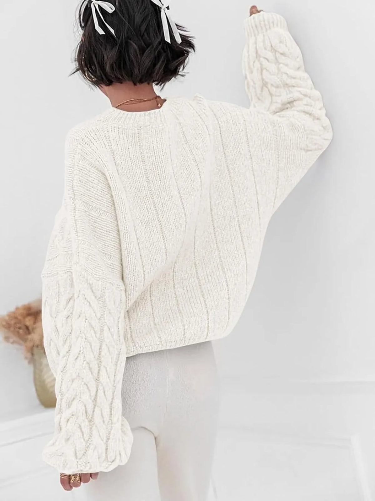 Back view of a model wearing a white cable knit long sleeve sweater, showcasing its textured design and relaxed fit.