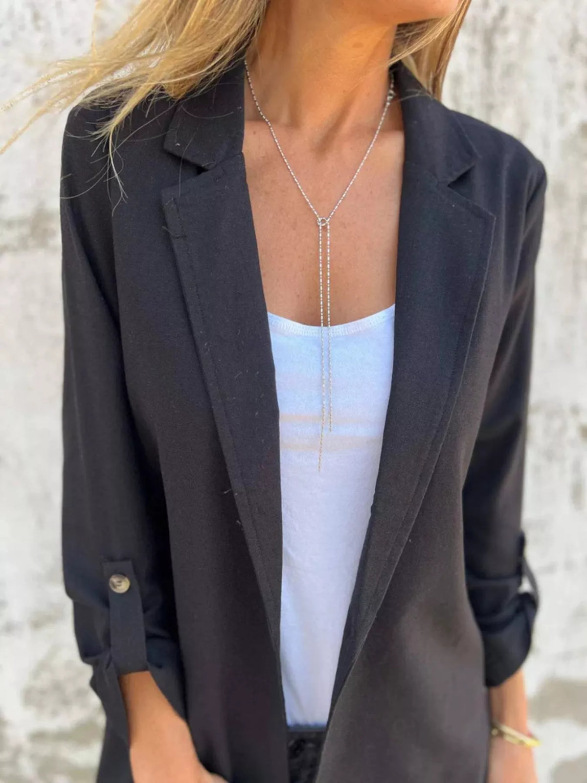 Woman wearing a black lapel collar long sleeve blazer over a white top, featuring a layered silver necklace.