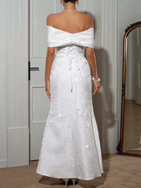 Back view of a woman in a white off-shoulder maxi dress featuring a lace-up design and fitted silhouette.