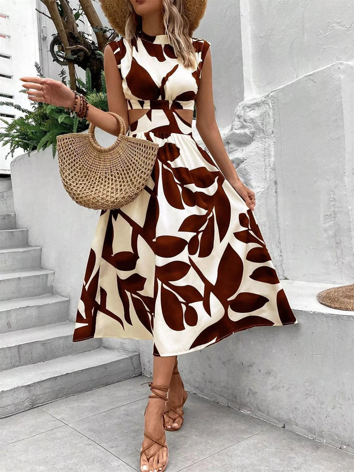 Stylish model wearing a cutout printed sleeveless dress with brown leaf patterns, holding a straw bag.