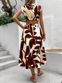 Back view of a woman in a brown and cream floral print sleeveless dress with a tied waist and flowy skirt.