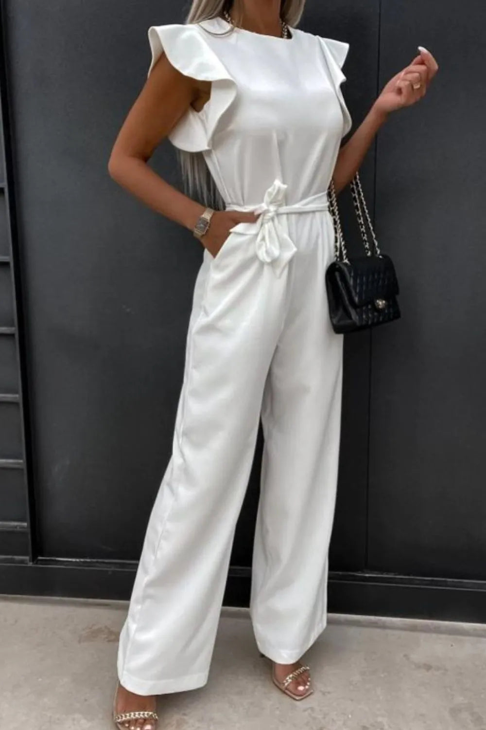 Model wearing a stylish white round neck cap sleeve jumpsuit with tied waist and flared pants.
