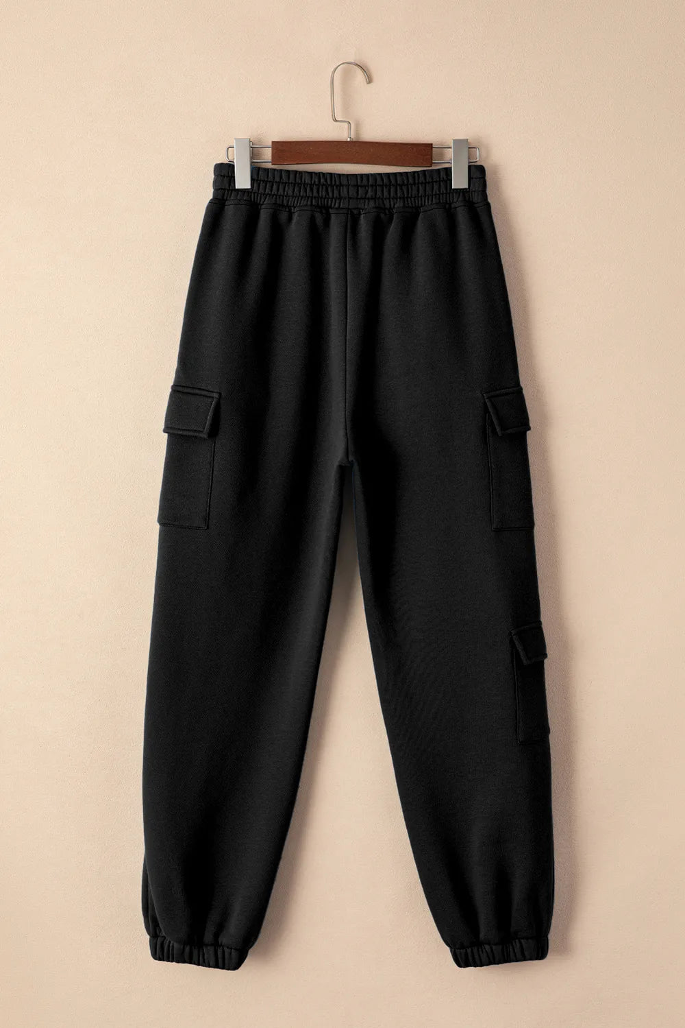 Black pocketed elastic waist joggers hanging on a hanger against a neutral background, ideal for affordable activewear.