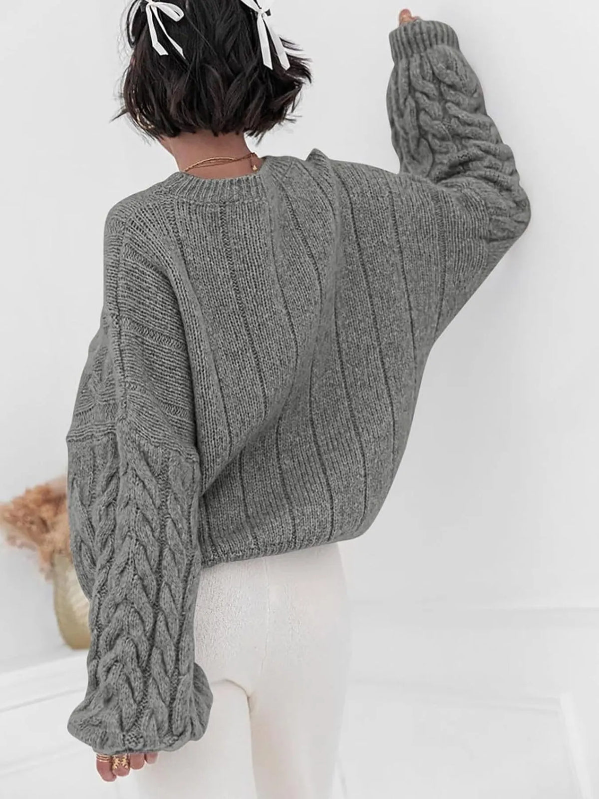 Back view of a model wearing a gray cable knit long sleeve sweater, showcasing its stylish, oversized fit.